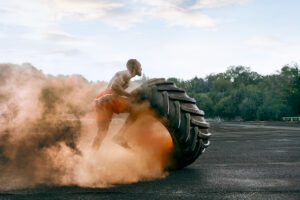 Handsome african american muscular man flipping burning big tire outdoor with smoke